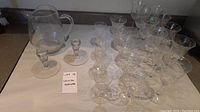 Photo showing the full collection of 23 crystal glassware items including glasses, pitcher, and candle holders displayed on a white cloth.