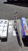 Galileo thermometer and barometer displayed standing outdoors, with box and styrofoam packaging beside it.