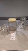 Four glass kitchen jars with various lids displayed on a surface with a label "Glass Kitchen Jars".
