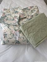 Queen size floral duvet cover, green duvet cover folded on top, floral pillow shams on white surface
