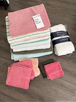 Stack of folded bath towels in various colors with folded white wrapped white face cloths and grouped colored face cloths in front.