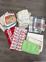 Lot of 18 kitchen towels and rags arranged in groups by pattern and color on a floor.