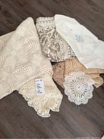 Overview photo showing the four tablecloths and four lace doilies arranged on wooden flooring, highlighting textures and colors.