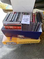 Two boxes containing mixed genre music CDs, showing spines and case fronts.