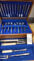 Full view of the flatware set in wooden box with blue velvet lining displaying the utensils arranged in slots.