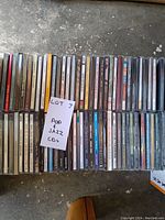 Top view of two rows of pop and jazz CDs in jewel cases with visible album spine titles, stored in a box.