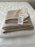 Stack of folded sheets and mattress cover with white note card showing lot information.