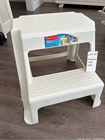 Photo showing the front and top view of the white Rubbermaid plastic step stool with label, measuring around 18.5 x 18.2 x 16 inches.