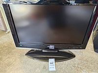 Front view of the Sharp Aquos 25-inch flatscreen TV showing the screen, bezel, and stand with a lot label in front.