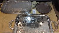 Three silver trays: two large rectangular trays with decorative engraving and handles, one medium round tray with pierced edge