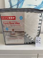 Front view of Skip Hop Playspot Geo foam floor tiles packaging showing product name, brand, and baby photo.