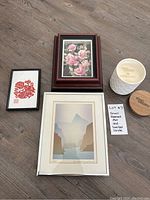 Photo showing all four items laid out on wood surface: three framed art pieces of different sizes and one white sandalwood scented candle with wooden lid removed.