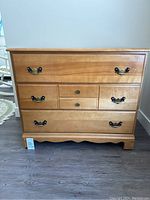 Front view of the wooden dresser showing three large drawers with brass handles and two smaller center drawers with round metal knobs, polished wood finish, and scalloped base detail.