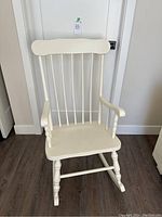 Front view of white wooden rocking chair with spindle backrest and curved armrests.