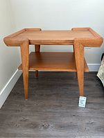 Front view of solid wood side table showing tapered legs, top surface with raised edges, and lower shelf.