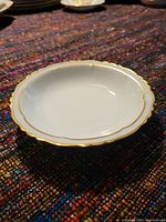 Top view of white fine bone china candy dish showing scalloped edges and gold trim, placed against a colorful textile background