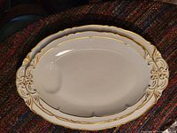 Two oval fine bone china platters with gold scalloped edges and indentation for sauce, stacked together to show relative size