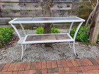 Front view of white metal console table with slate tiles on top and wood tiles on bottom shelf in outdoor setting.