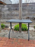 Gray metal table outdoors on gravel with brick and wood fence background