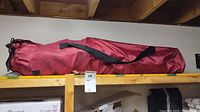Shelf with three red camping chair carry bags stacked horizontally in storage area.