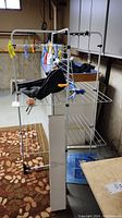 Vinyl coated deluxe tower clothes dryer with clothespins and black clothespin bag hanging on it in basement setting