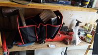 Hydraulic trolley jack beside a black and orange car storage bag with reflective sunshade and various tools on a shelf