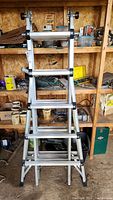 Front view of aluminum telescopic articulated ladder in folded position showing rungs, hinge joints, and rubber feet.