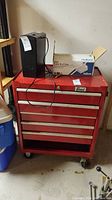 Photo of red metal tool box with a black shredder and a Nutone box on top, showing the full front side with drawers and casters.