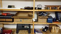 Shelf view with Rubbermaid plastic step stool/toolbox, toolboxes, storage bins, cardboard boxes containing screws and other hardware, and assorted hand tools.