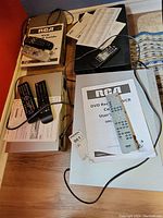 Top view of multiple VCR units with remotes and manuals placed on them, showing RCA DVD Recorder/VCR combo and other VCR units