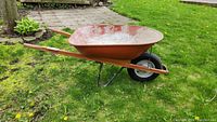 Side view of the wheelbarrow showing metal basin, wooden handles, tire, and metal legs.