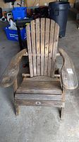 Full view of the wood folding Adirondack chair showing weathered slatted wood with wide arm rests and curved back slats.