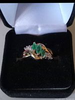 Ring in open black velvet box showing three marquise emeralds flanked by diamonds, twisted gold band