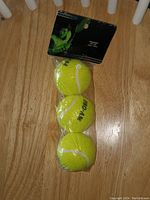 Front view of three Pro-Am branded yellow tennis balls in sealed plastic packaging lying flat on a wooden surface, with packaging card showing a tennis player image on top.