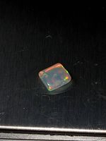 Close-up of the polished square fire opal on a black surface showing its rainbow colors and shine.