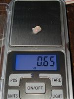 Small polished opal chunk on digital scale showing weight of 0.65 carats.