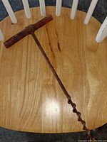 Top-down view of the antique barn beam auger on wooden chair seat, showing rusted spiral bit and worn wooden T-handle.