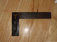 Antique iron and brass wood block square tool placed on wood surface, showing L-shape and patina on iron blade with brass handle
