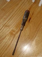 Full view of antique screwdriver showing wooden handle and metal shaft on wood floor.