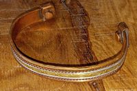 Close-up image of an adjustable copper balance bracelet with a brass braided design inset, resting on a wooden surface.