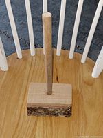 Full view of the ash wood paper towel holder on a wooden chair seat showing the live edge bark on the base and cylindrical wood rod