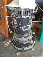 Front and side view of dusty used kerosene heater showing vent slots, control knob, and attached stainless steel grill deflector sides.