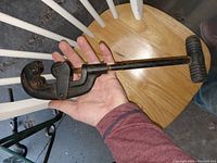 Photo showing a large antique pipe cutter on a hand, demonstrating size and design with an adjustable jaw and turn handle.