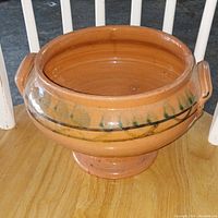 Overall clear view of the pottery bowl showing shape, handles, and pedestal base on wooden surface.