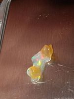 Photo of larger fire opal chunk showing two-tone yellow coloring and vibrant rainbow play of color on a wooden background.