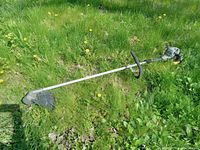 Full view of Ryobi gas weed wiper trimmer lying on grass, showcasing full length and components.