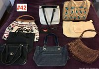 Full lot of seven assorted handbags displayed on dark surface showing various styles, colors, and materials