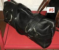 Black leather handbag side view showing zipper, handle, and metal ring details.