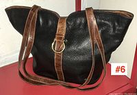 Side view of the Furla handbag showing black leather body with brown leather trim and gold buckle detail.