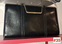 Front view of black leather clutch handbag with gold-tone metal handle at the top.
